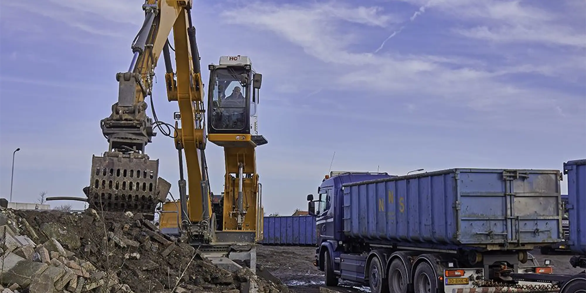 Excavator loading demolition debris into a dump truck on an ACH Services job site in Bakersfield
